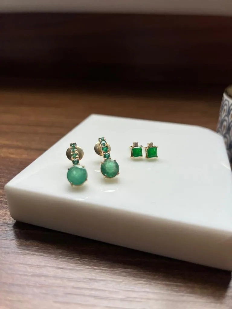 Brincos de ouro com esmeraldas e jade sobre bloco de mármore
